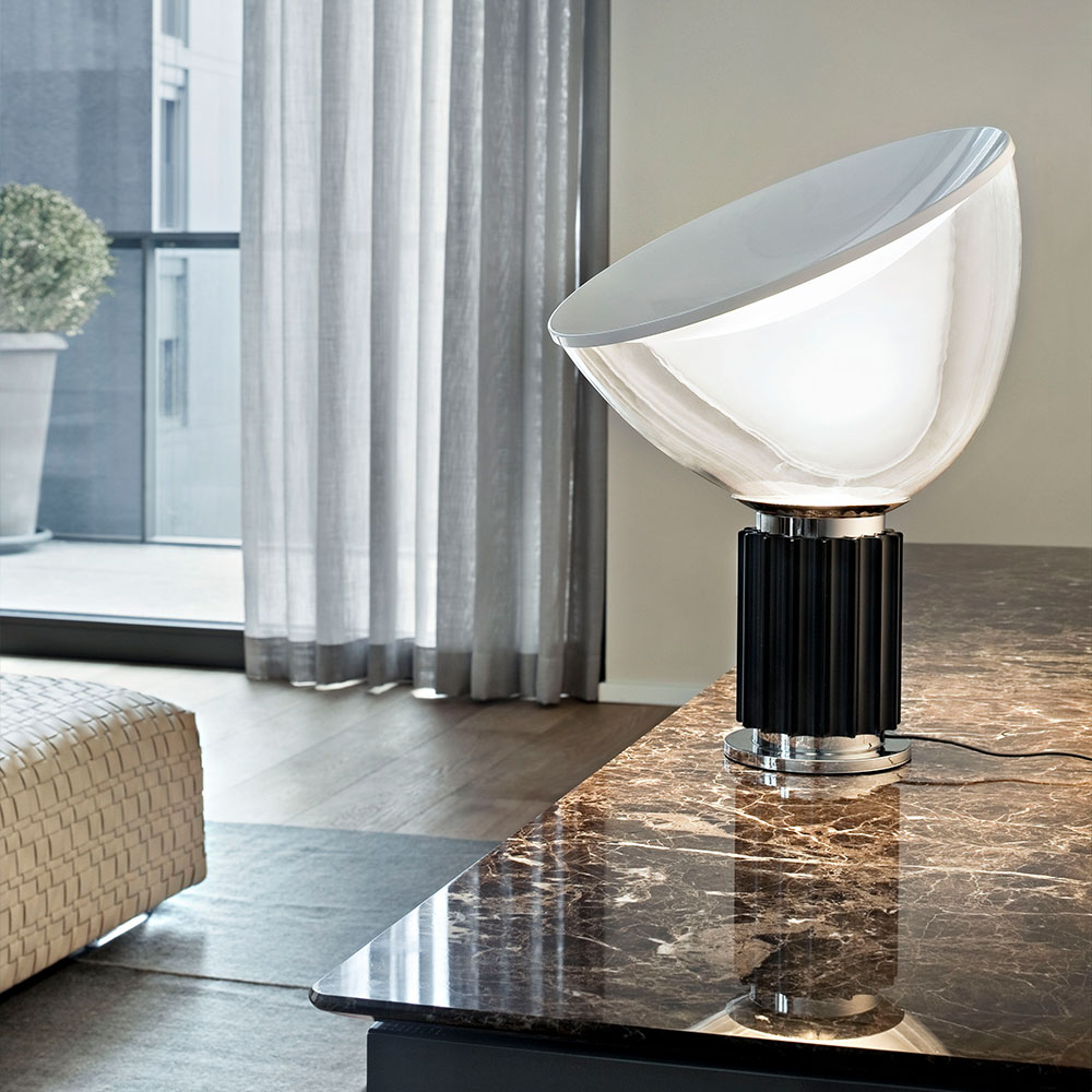 FLOS Taccia Tischleuchte bei lampenonline.de. Die FLOS Taccia LED-Tischleuchte überträgt die Formensprache der 60er Jahre gekonnt in die Moderne. Ihr markantes Merkmal ist der ausladende Diffusor aus mundgeblasenem, transluzentem Glas. 